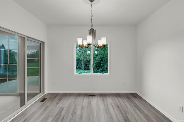 empty room with baseboards, a chandelier, a wealth of natural light, and wood finished floors