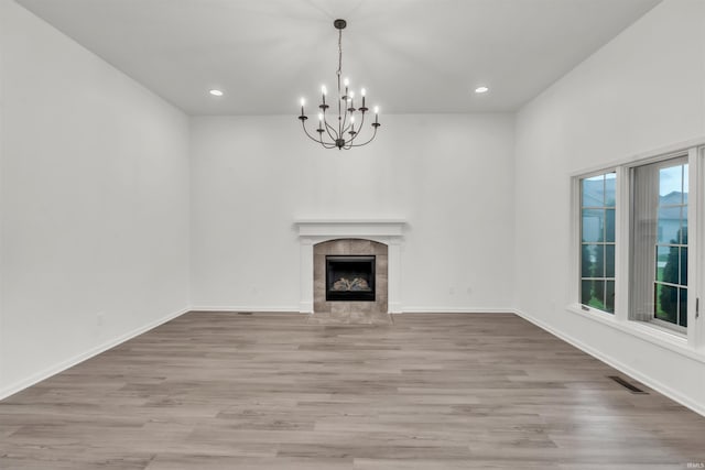 unfurnished living room featuring a tiled fireplace, light wood-style floors, and a notable chandelier