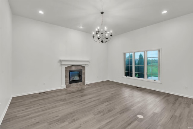 unfurnished living room with an inviting chandelier, baseboards, wood finished floors, and a tiled fireplace
