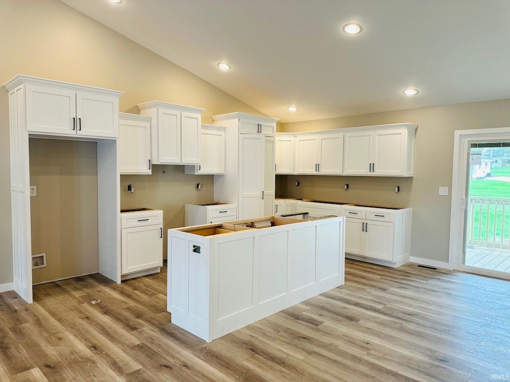 kitchen featuring vaulted ceiling, white cabinets, a kitchen island, and light wood-type flooring