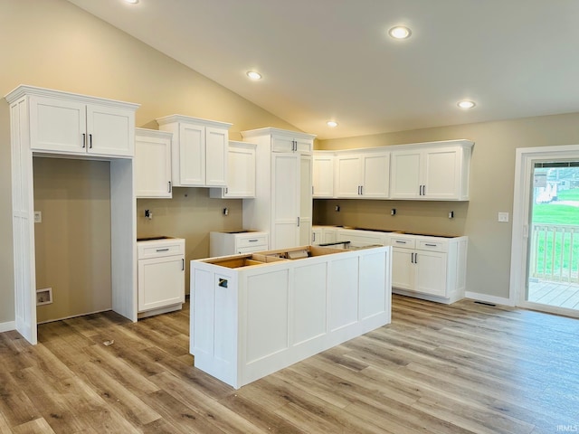 kitchen featuring vaulted ceiling, white cabinets, a kitchen island, and light wood-type flooring