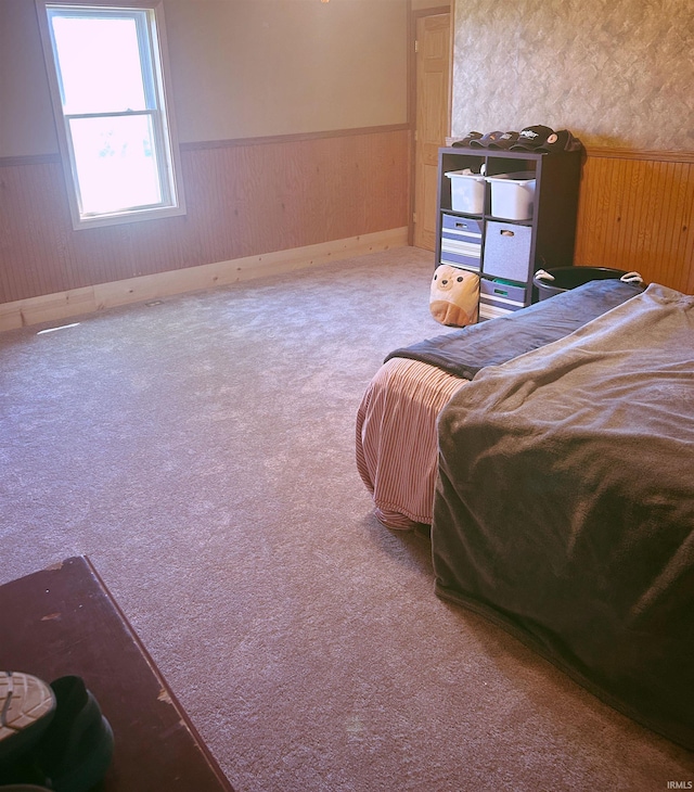 carpeted bedroom with a wainscoted wall and wood walls