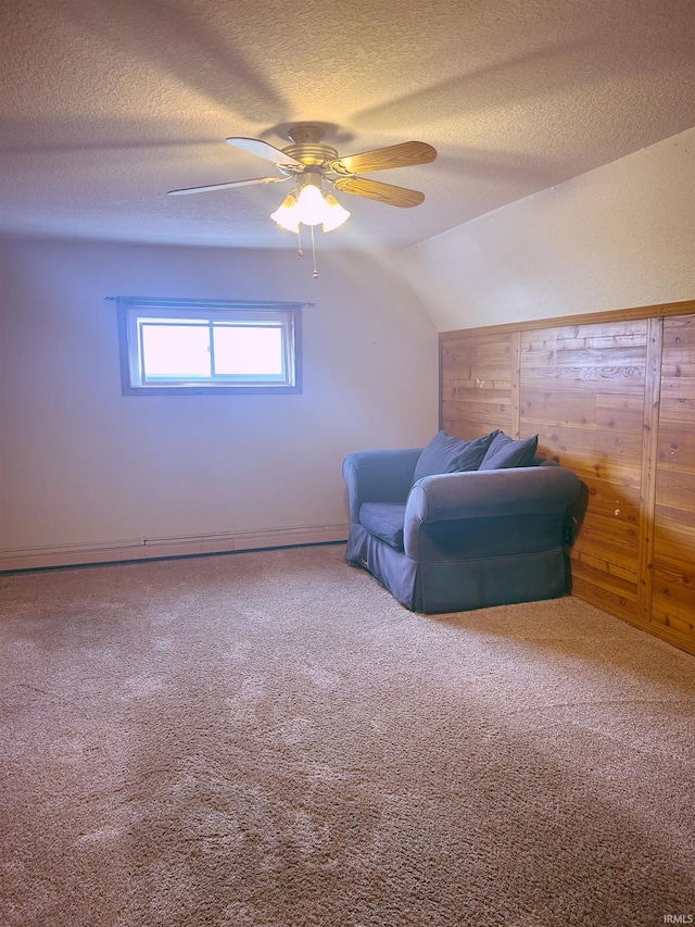 living area with ceiling fan, carpet, vaulted ceiling, and a textured ceiling