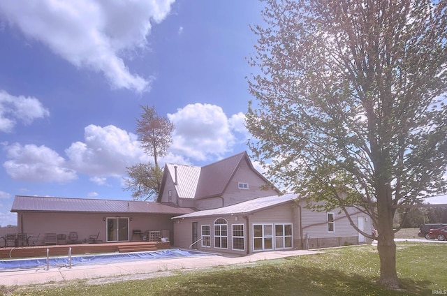 rear view of house featuring a yard, a deck, metal roof, and a covered pool