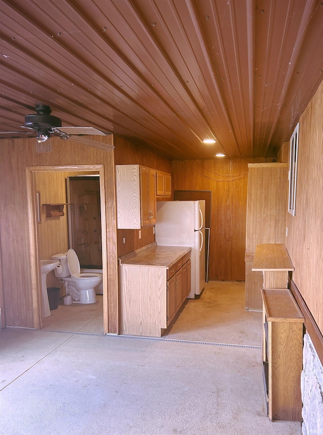 kitchen featuring wooden walls, a ceiling fan, freestanding refrigerator, and light countertops