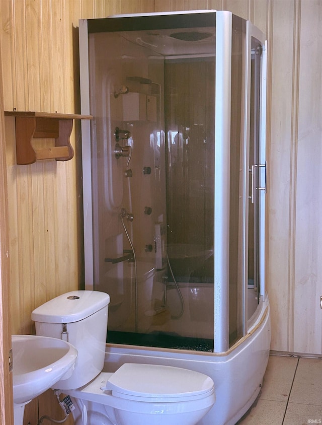 bathroom with wooden walls, a shower stall, toilet, and a sink