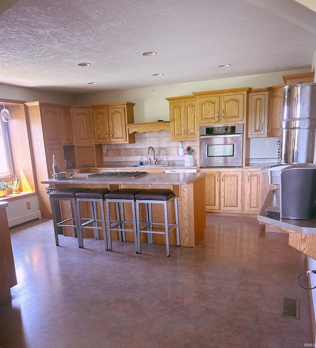 kitchen with a kitchen breakfast bar, a center island, a textured ceiling, a sink, and appliances with stainless steel finishes
