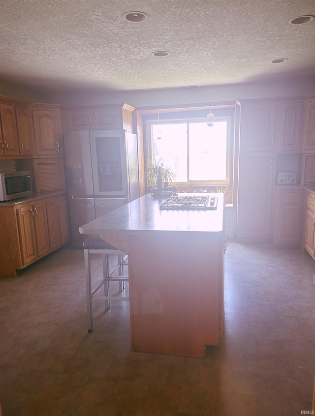 kitchen with a kitchen island, a textured ceiling, stainless steel microwave, and a kitchen bar