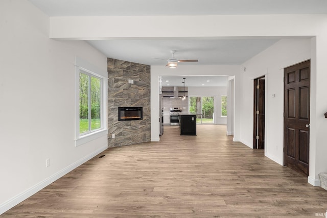 unfurnished living room with light wood-style floors, a ceiling fan, baseboards, and plenty of natural light