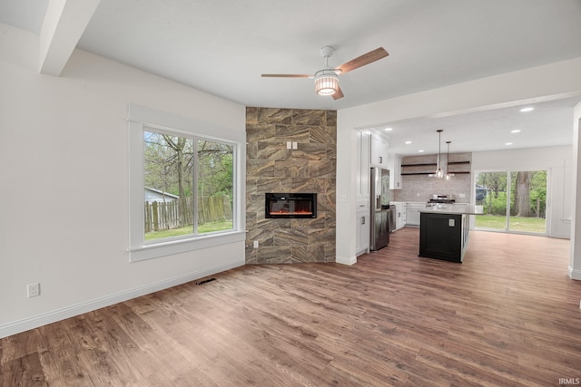 unfurnished living room with ceiling fan, visible vents, a wealth of natural light, and wood finished floors