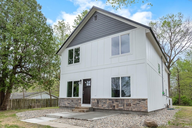 back of house featuring fence, board and batten siding, entry steps, and stone siding