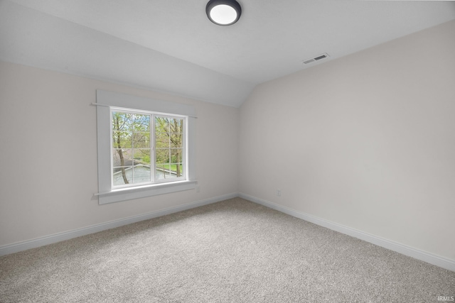 carpeted empty room featuring baseboards, visible vents, and vaulted ceiling