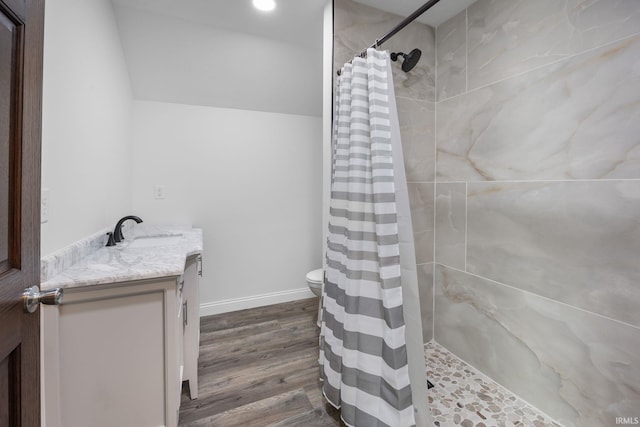 full bath featuring vanity, wood finished floors, toilet, baseboards, and tiled shower