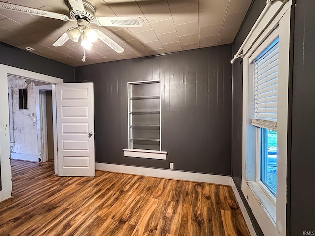 empty room featuring baseboards, ceiling fan, wood finished floors, and a wealth of natural light