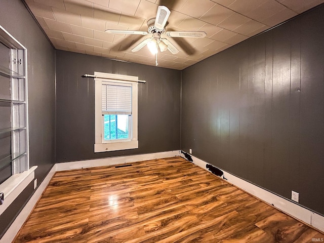empty room featuring wooden walls, a ceiling fan, wood finished floors, and visible vents