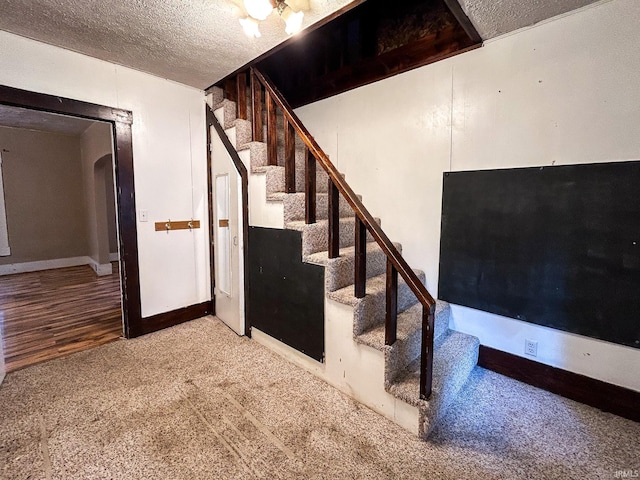 staircase featuring carpet floors, a textured ceiling, and baseboards