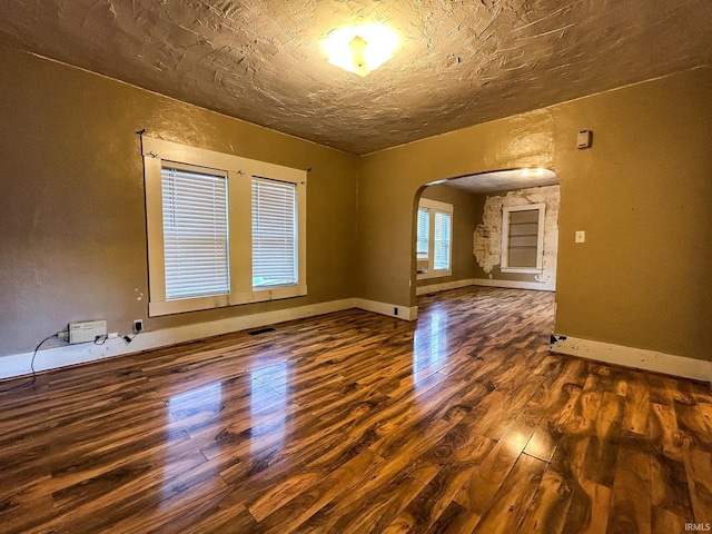 empty room featuring arched walkways, baseboards, a textured wall, and wood finished floors