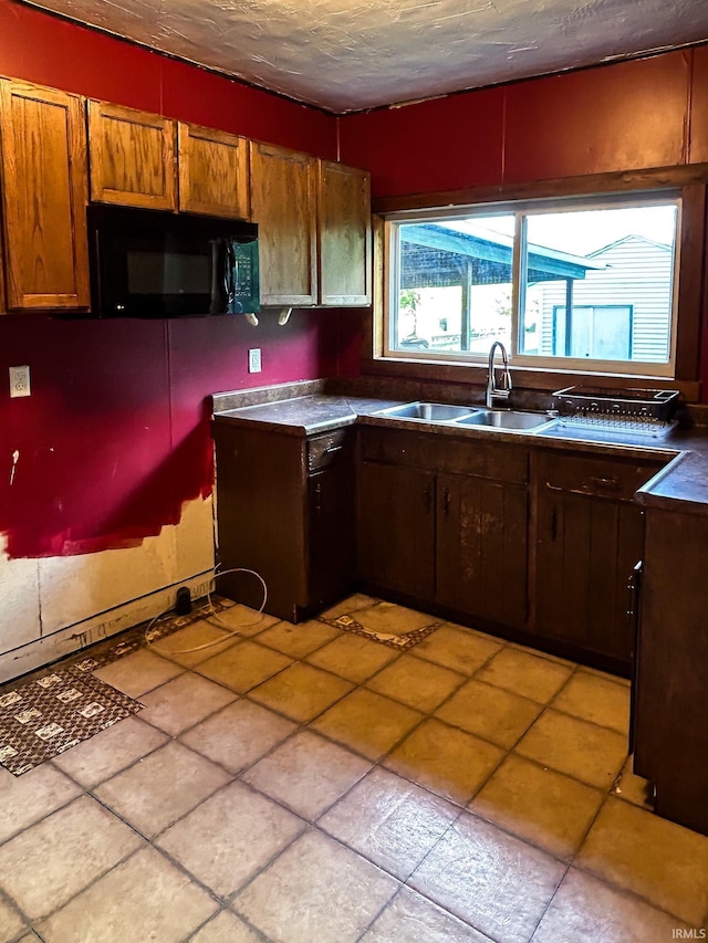 kitchen with light tile patterned flooring, black microwave, dark countertops, a textured ceiling, and a sink