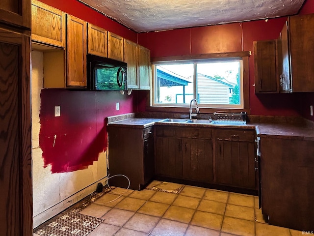 kitchen featuring a textured ceiling, black microwave, dark countertops, and a sink