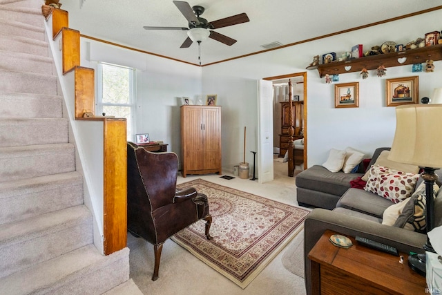 living room with a ceiling fan, light colored carpet, visible vents, ornamental molding, and stairs