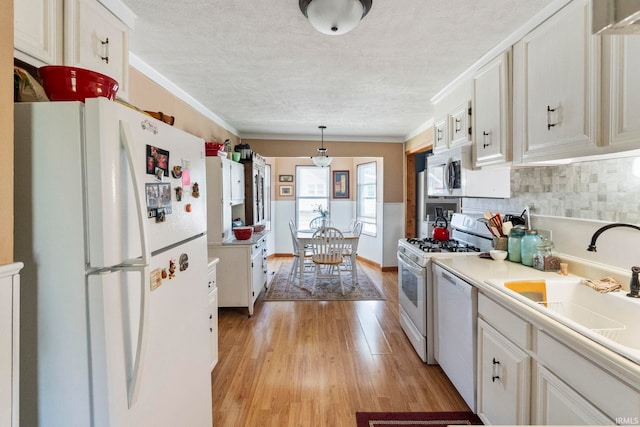 kitchen with decorative backsplash, a textured ceiling, a sink, light wood finished floors, and white appliances