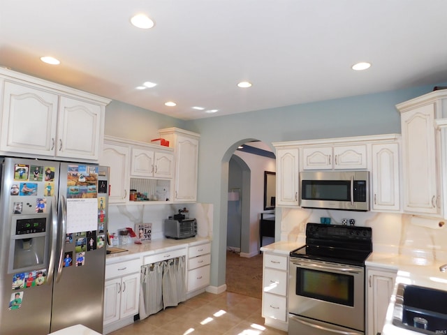 kitchen featuring appliances with stainless steel finishes, arched walkways, light countertops, recessed lighting, and light tile patterned flooring