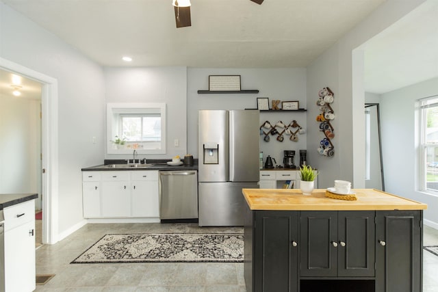 kitchen with appliances with stainless steel finishes, a sink, white cabinetry, baseboards, and butcher block counters