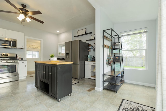 kitchen with ceiling fan, wooden counters, baseboards, white cabinets, and stainless steel appliances