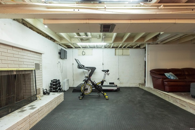 workout area featuring concrete block wall, a brick fireplace, and dark carpet