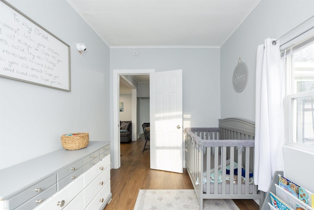 bedroom with a nursery area, ornamental molding, and wood finished floors