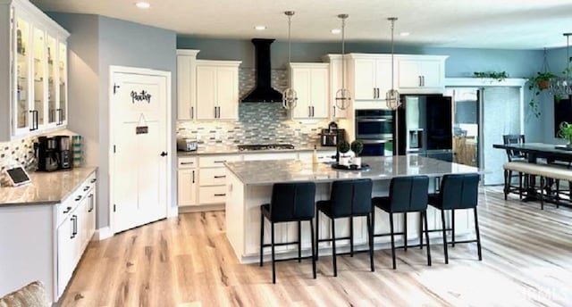 kitchen featuring wall chimney exhaust hood, white cabinets, tasteful backsplash, light wood-style flooring, and stainless steel appliances