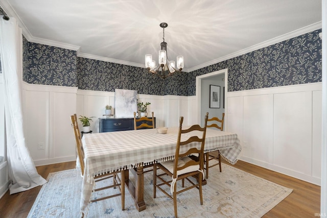dining space featuring crown molding, a notable chandelier, wood finished floors, and a decorative wall