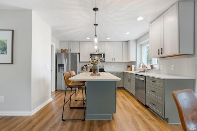 kitchen featuring light countertops, gray cabinets, a sink, light wood-style flooring, and appliances with stainless steel finishes