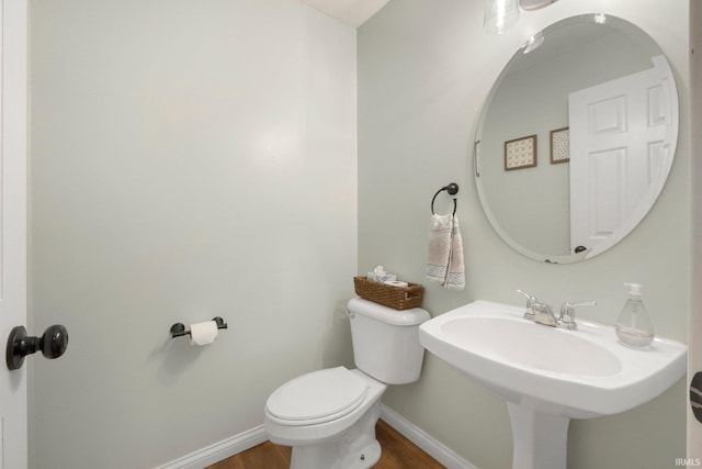 bathroom featuring baseboards, wood finished floors, and toilet