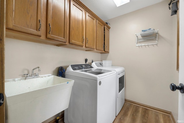 laundry area featuring cabinet space, a sink, baseboards, wood finished floors, and washing machine and dryer