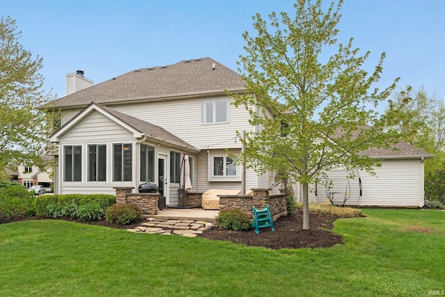 rear view of property featuring a shingled roof, a sunroom, a chimney, a patio area, and a yard