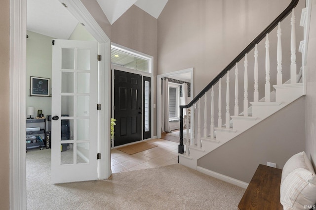 tiled foyer entrance with baseboards, carpet, stairs, and a towering ceiling