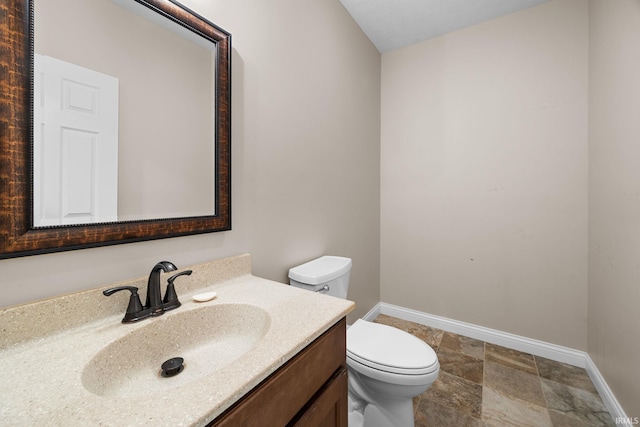 bathroom featuring toilet, baseboards, stone finish floor, and vanity