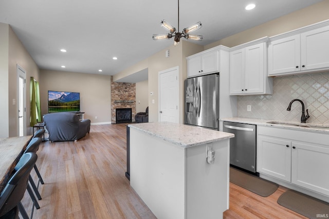 kitchen featuring decorative backsplash, a stone fireplace, a center island, a sink, and stainless steel appliances