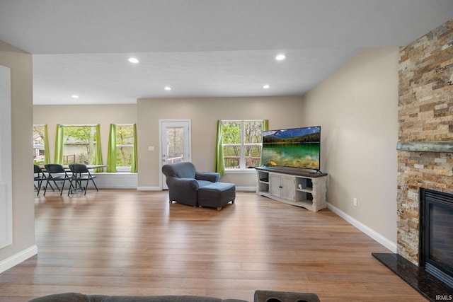 living room featuring a stone fireplace, recessed lighting, baseboards, and wood finished floors