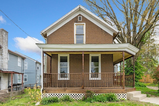 view of front of home featuring a porch, brick siding, and fence