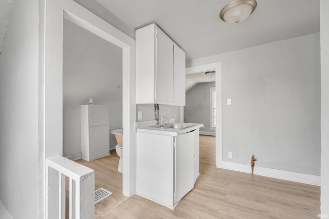 laundry area with a sink, baseboards, light wood-type flooring, and visible vents