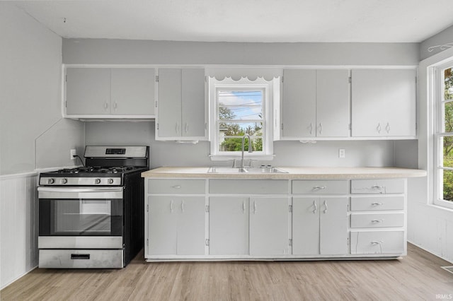 kitchen with a sink, light countertops, stainless steel gas range, and light wood-style flooring