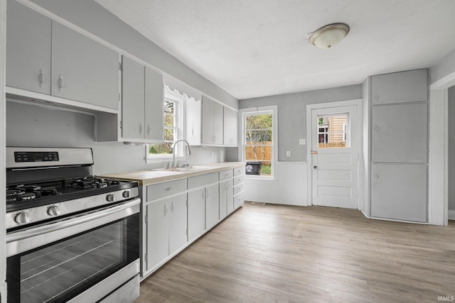 kitchen with wainscoting, a sink, light wood finished floors, stainless steel range with gas cooktop, and under cabinet range hood