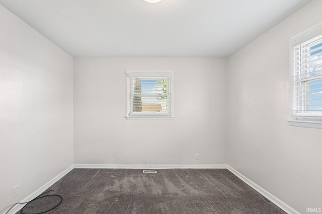 empty room with baseboards, visible vents, and dark colored carpet