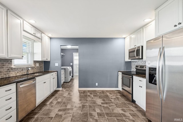 kitchen featuring washing machine and clothes dryer, a sink, baseboards, white cabinets, and stainless steel appliances