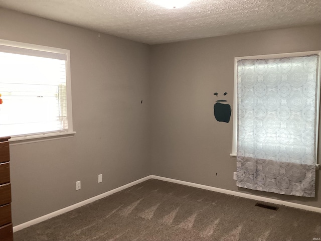 unfurnished room featuring visible vents, a textured ceiling, baseboards, and dark colored carpet