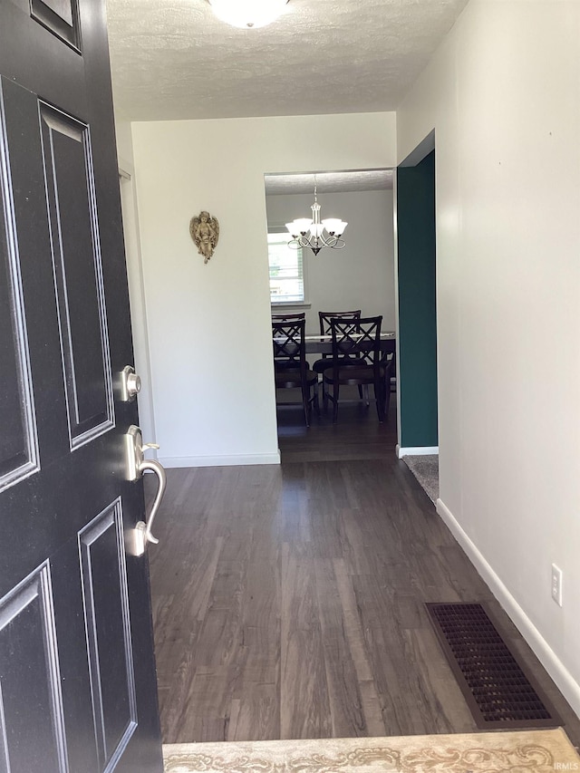 entrance foyer featuring a textured ceiling, a chandelier, dark wood finished floors, baseboards, and visible vents