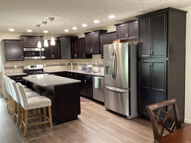 kitchen with backsplash, appliances with stainless steel finishes, a center island, light wood-type flooring, and a sink