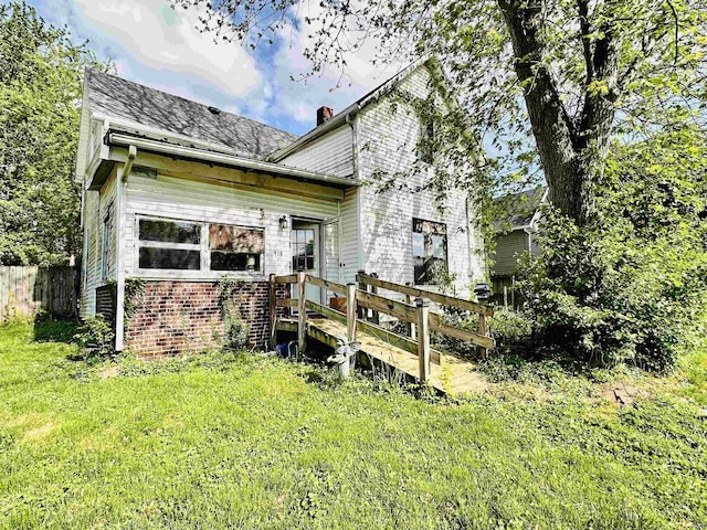 back of property featuring a chimney, a wooden deck, brick siding, fence, and a yard